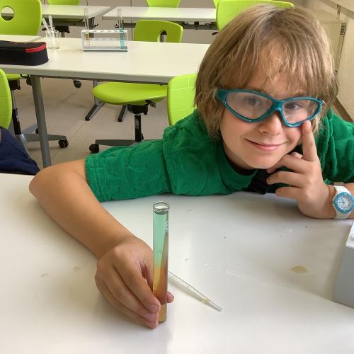 Kind mit einem Reagenzglas mit mehreren farbigen Flüssigkeitsschichten