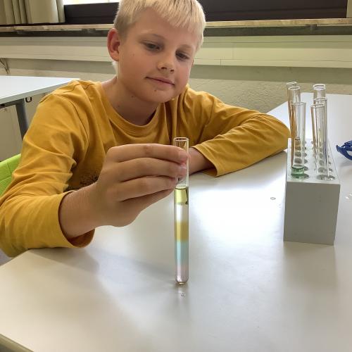 Kind mit farbigen Flüssigkeitsschichten in einem Reagenzglas