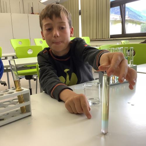 Kind mit farbigen Flüssigkeitsschichten in einem Reagenzglas