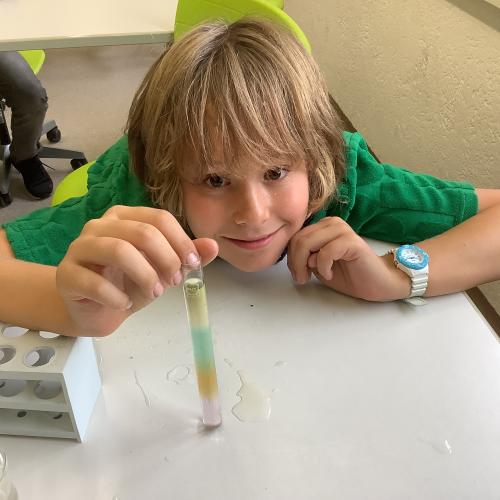 Kind mit farbigen Flüssigkeitsschichten in einem Reagenzglas