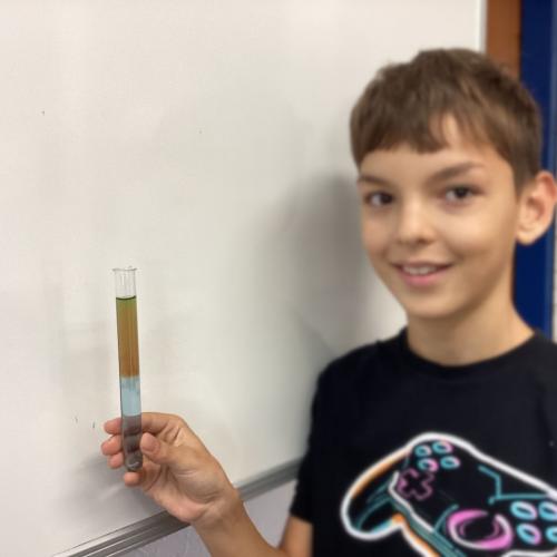 Kind mit Reagenzglas, in dem sich übereinander geschichtete Flüssigkeiten befinden.