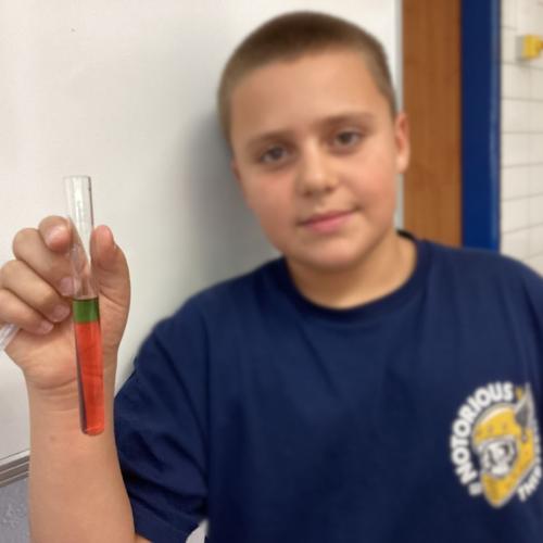 Kind mit Reagenzglas, in dem sich übereinander geschichtete Flüssigkeiten befinden.