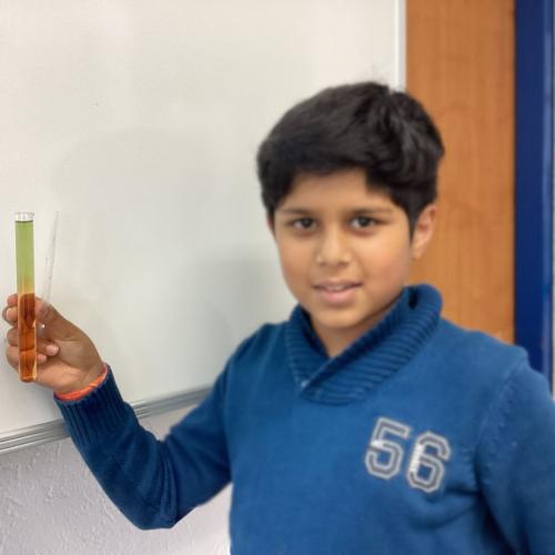 Kind mit Reagenzglas, in dem sich übereinander geschichtete Flüssigkeiten befinden.