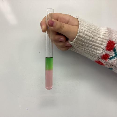 Kind mit Reagenzglas, in dem sich übereinander geschichtete Flüssigkeiten befinden.