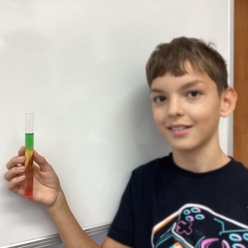 Kind mit Reagenzglas, in dem sich übereinander geschichtete Flüssigkeiten befinden.