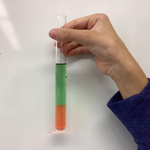 Kind mit Reagenzglas, in dem sich übereinander geschichtete Flüssigkeiten befinden.