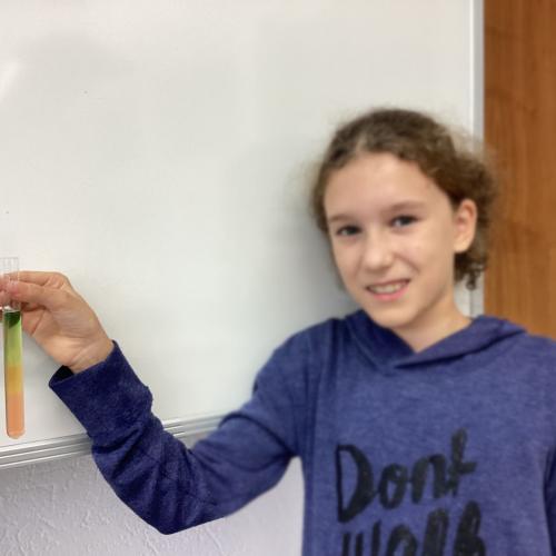 Kind mit Reagenzglas, in dem sich übereinander geschichtete Flüssigkeiten befinden.