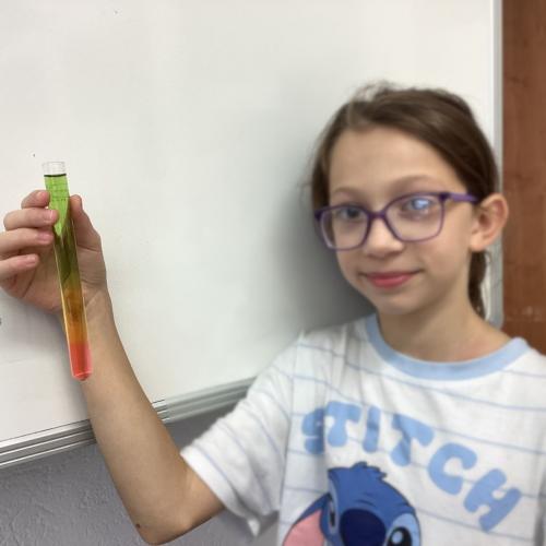 Kind mit Reagenzglas, in dem sich übereinander geschichtete Flüssigkeiten befinden.