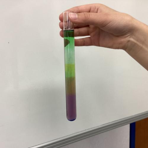 Kind mit Reagenzglas, in dem sich übereinander geschichtete Flüssigkeiten befinden.