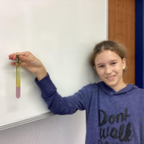 Kind mit Reagenzglas, in dem sich übereinander geschichtete Flüssigkeiten befinden.