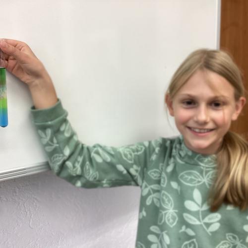 Kind mit Reagenzglas, in dem sich übereinander geschichtete Flüssigkeiten befinden.