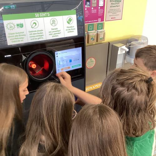 Kinder füllen einen Pfandautomaten mit selbst gesammelten PET-Flaschen.