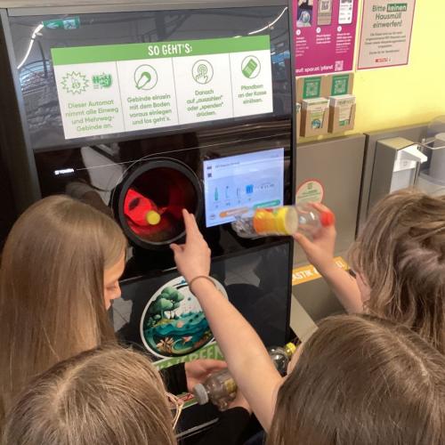 Kinder füllen einen Pfandautomaten mit selbst gesammelten PET-Flaschen.