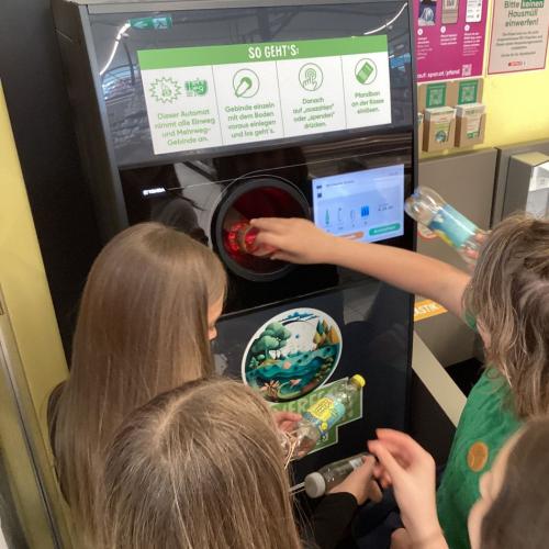 Kinder füllen einen Pfandautomaten mit selbst gesammelten PET-Flaschen.