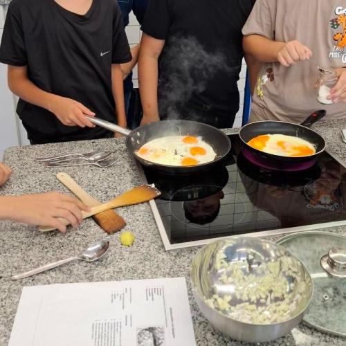 Kinder kochen Spiegeleier in der Schulküche.