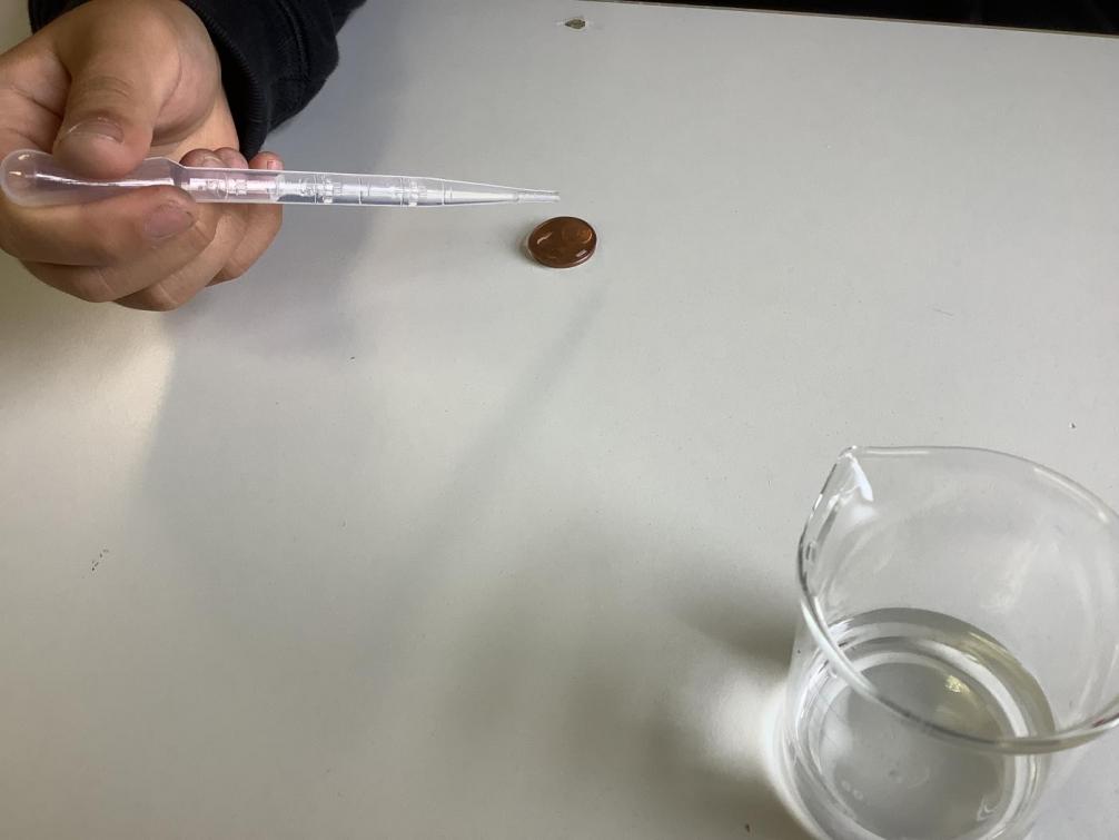 Ein Kind tropft mit einer Plastikpipette Wasser auf eine 5-Cent-Münze