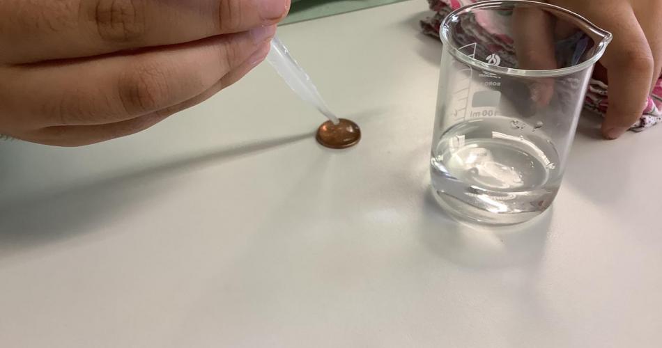 Wassergefülltes Becherglas und Münze mit Wasserberg drauf