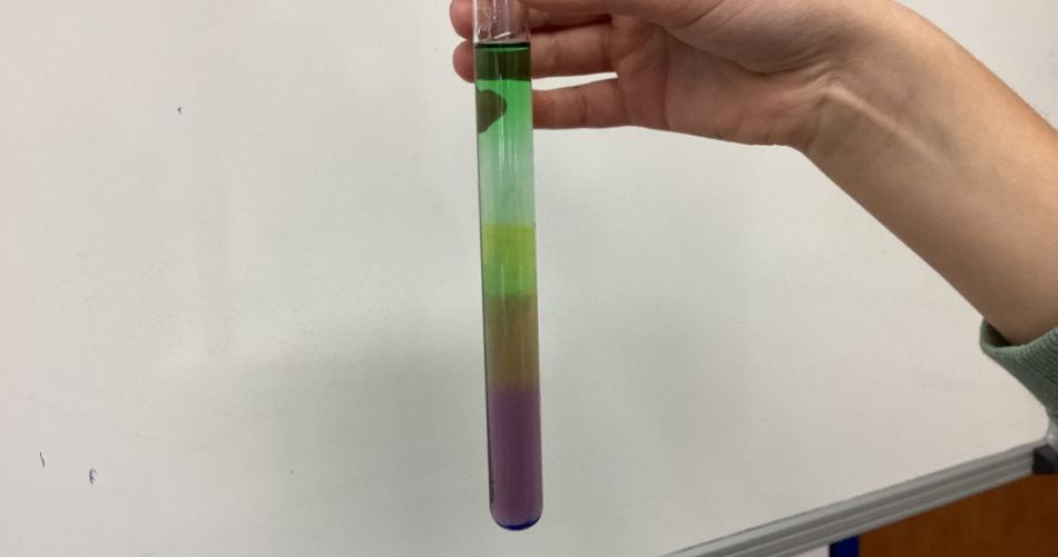 Kind mit Reagenzglas, in dem sich übereinander geschichtete Flüssigkeiten befinden.